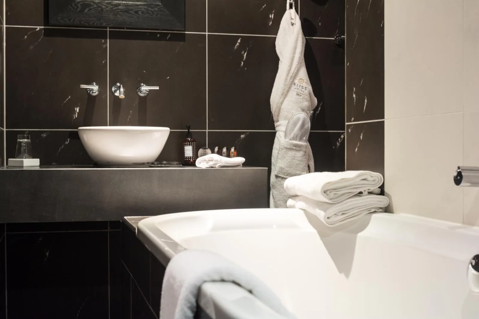 Badkamer met zwart marmer, witte opzetwastafel, ligbad en badjas aan de haak