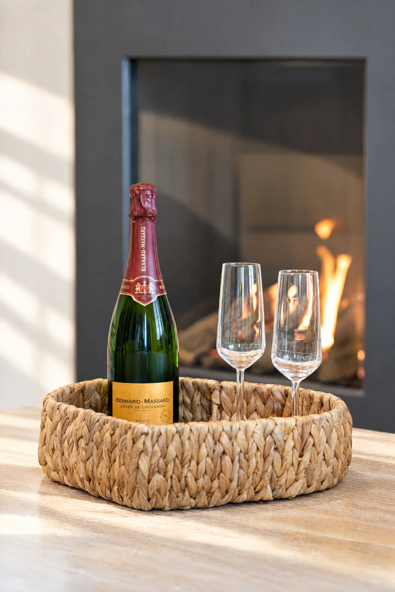 Fles champagne en twee glazen in een rieten schaal voor de brandende haard