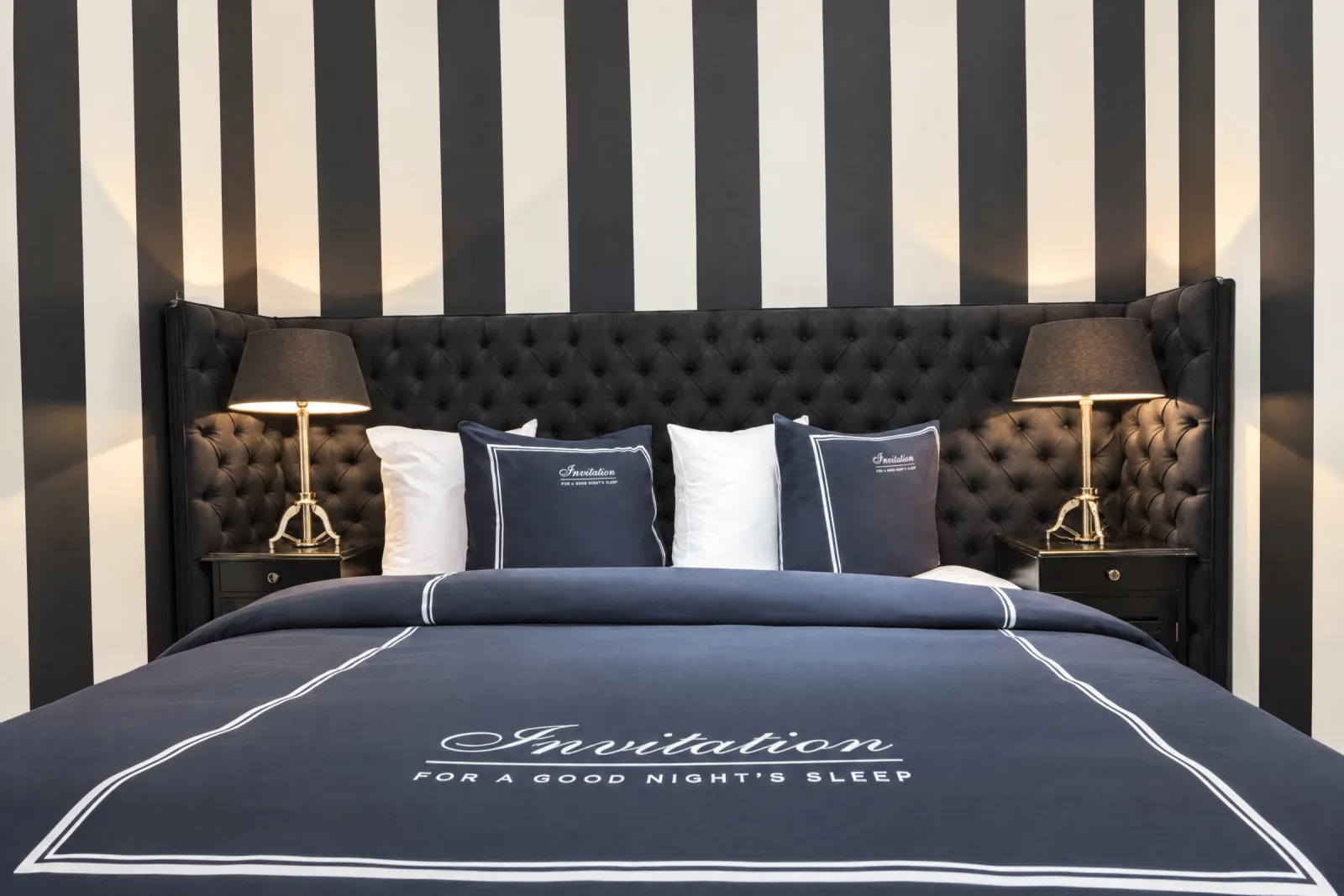 Bed met zwart capitonné hoofdbord voor de gestreepte wand van de Black & White Suite