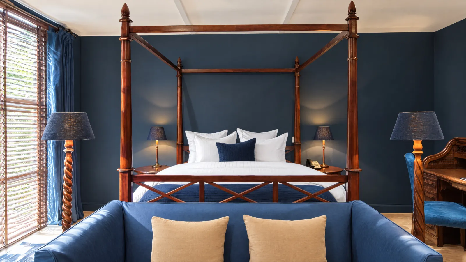 Mahoniehouten hemelbed met een blauwe bank ervoor in de Colonial Suite