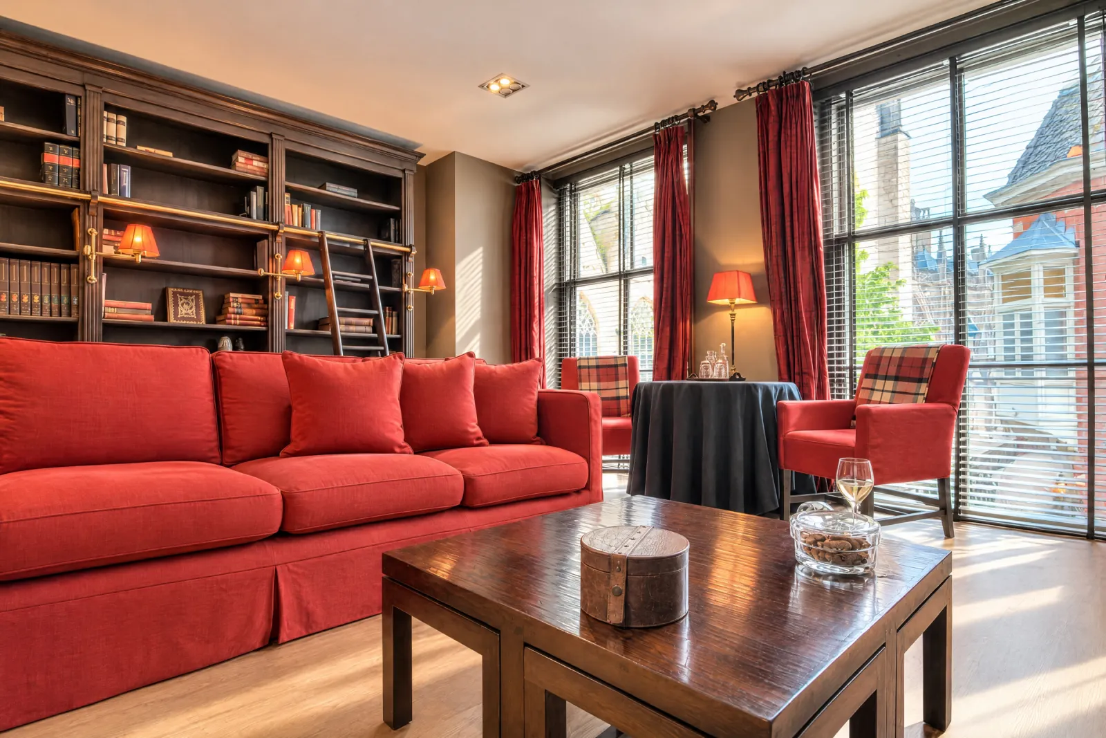 Rode bank en boekenkast tot het plafond met ladder in de Dickens & Jones Suite