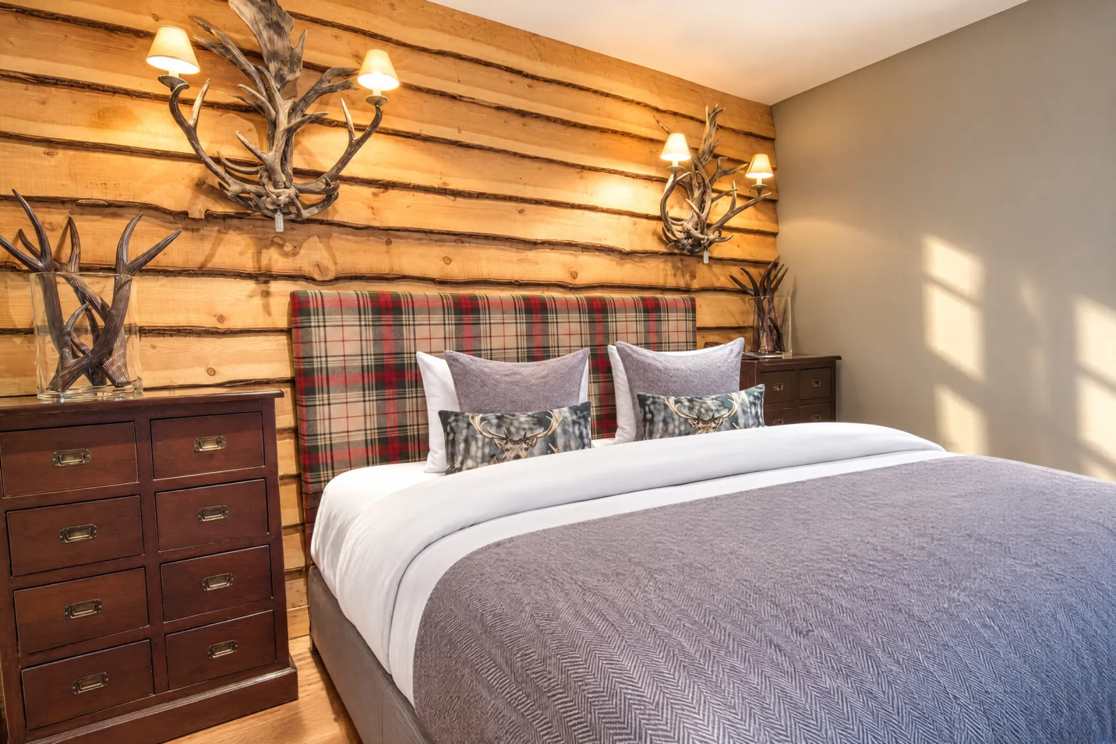 Bed met tartan hoofdbord tegen een houten wand met geweien in de Lodge Suite
