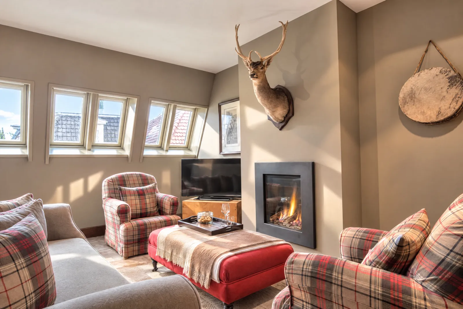 Zithoek met tartan fauteuils, rode poef en gashaard onder de dakkapellen van de Lodge Suite